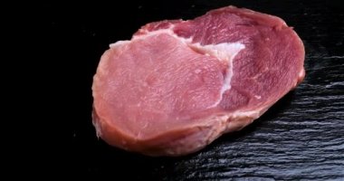 Siyah taşın üzerinde dönen bir parça çiğ et. Sağlıklı bir diyete hazır taze et. Et kaynağı protein. Dolly 4K çekti.