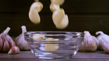 Fresh garlic clove peeled falling in glass bowl. The raw garlic is one of the most popular ingredients of the basic recipes with nutritional properties, infamous aroma and health benefits. Slow motion