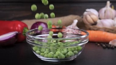 Frozen peas falling into a glass bowl with vegetables in background. Peas are a good source of vitamins C and E, zinc, and other antioxidants that strengthen the immune system. Healthy food concept. Slow motion