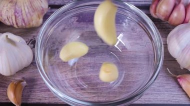 Fresh garlic clove peeled falling into glass bowl. The raw garlic is one of the most popular ingredients of the basic recipes with nutritional properties, infamous aroma and health benefits. Slow motion