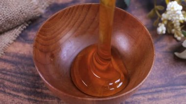 Honey pouring into a wooden bowl in slow motion. Honey contains many nutrients, antioxidants, improves heart health, wound care, offers antidepressant and anti-anxiety benefits.