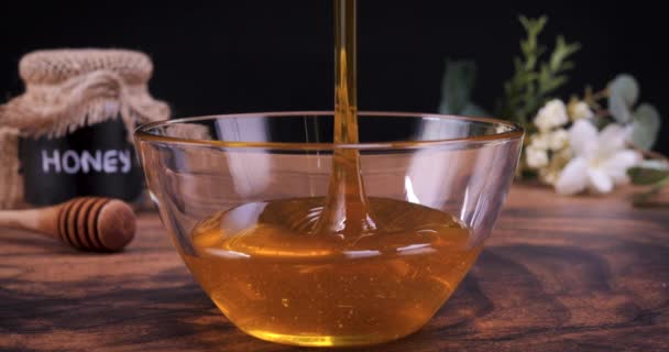 蜂蜜を木製のテーブルの上に透明なボウルに注いだ 蜂蜜は多くの栄養素 抗酸化物質が含まれており 心臓の健康 創傷ケアを改善し 抗うつ薬と抗不安効果を提供しています — ストック動画