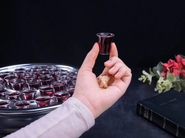 Closeup of young woman taking communion the wine symbol of Jesus Christ blood in small cups on black background. Easter Passover and Lord Supper concept.