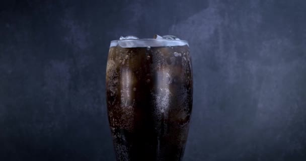 氷と泡とクールなコーラの飲み物 新鮮な冷たい甘い飲み物が氷のキューブの上に注がれました ブラックに夏のリフレッシュを施したコーラグラス ガラス回転4K — ストック動画