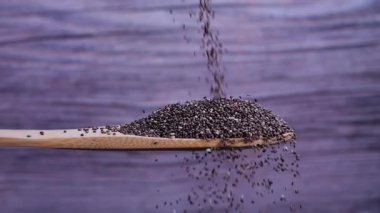 Chia tohumları gri arka planda tahta bir kaşığa düşer. Chia tohumları mineral, omega 3 yağ, antioksidan ve lif açısından zengindir. Sağlıklı gıda konsepti. Yavaş çekim