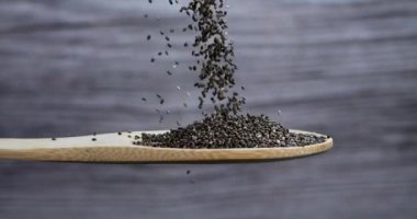 Chia tohumları gri arka planda tahta bir kaşığa düşer. Chia tohumları mineral, omega 3 yağ, antioksidan ve lif açısından zengindir. Sağlıklı gıda konsepti. 4k
