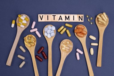 Ahşap kaşıklardaki farklı vitaminler ve gri arka planda yazılar. Haplar, uyuşturucular, ilaveler, ilaçlar, eczane ve sağlık hizmetleri kavramı.