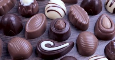 Kahverengi arka planda sütlü ve koyu çikolatalı pralinler. Çikolata ve tatlı tüketim konseptini sevmek. Dolly 4K çekti.