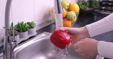 Kadın elleri mutfakta kırmızı dolma biber yıkıyor. Sağlıklı çiğ organik yiyecekler, vitaminler, böcek ilacı konseptinden sebze yıkamak. Yavaş çekim 4k