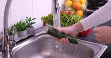 Kadın elleri mutfakta taze salata hazırlamak için salatalık yıkıyor. Sağlıklı çiğ organik yiyecekler, vitaminler, böcek ilacı konseptinden sebze yıkamak. Yavaş çekim 4k