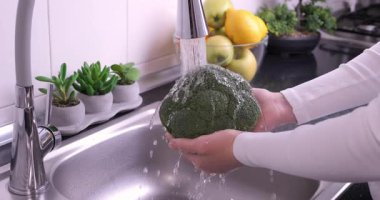 Kadın elleri mutfakta taze brokoli yıkıyor. Sağlıklı çiğ organik yiyecekler, vitaminler, böcek ilacı konseptinden sebze yıkamak. Yavaş çekim 4k