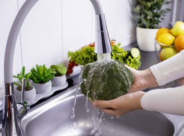 Kadın elleri mutfakta taze brokoli yıkıyor. Sağlıklı çiğ organik yiyecekler, vitaminler, böcek ilacı konseptinden sebzeleri yıkamak.. 