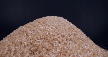 Esmer kamış şekeri siyah arkaplana döküldü. Çeşitli ürünlerde aşırı şeker içeriyor. Beslenmek. Sağlık kavramına yönelik şeker tüketiminin faydaları veya tehlikesi