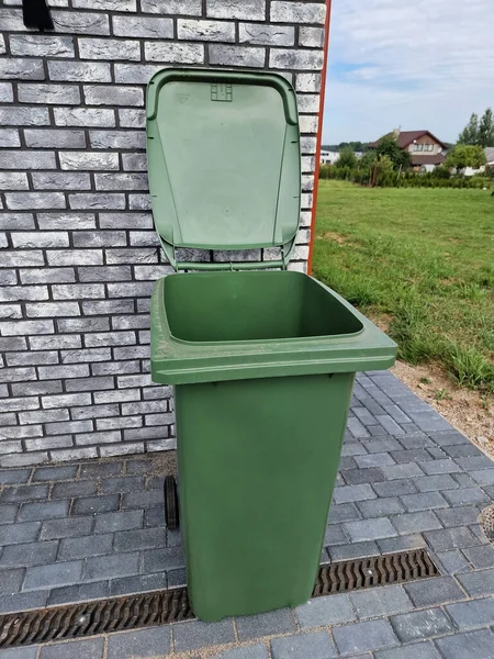 Empty green plastic trash garbage bin container for individual use in front of the modern house