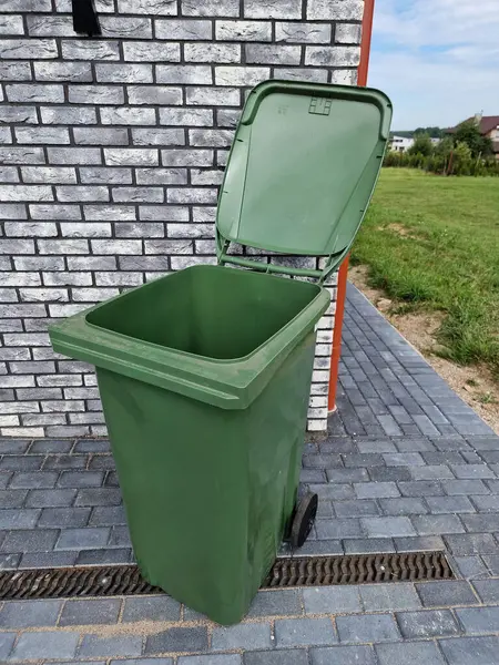 Empty green plastic trash garbage bin container for individual use in front of the modern house