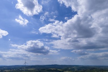Pofuduk beyaz bulutlarla kaplı berrak mavi bir gökyüzünün çarpıcı manzarası, dingin bir manzaraya bakan yuvarlanan tepeler ve bir rüzgar türbini, sükuneti göstermek için mükemmel..