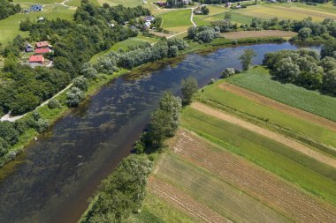Bereketli yeşil tarlalar ve ağaçlar arasında süzülen sakin bir nehrin havadan görünüşü kırsal manzaraları ve tarım güzelliklerini gözler önüne seriyor..