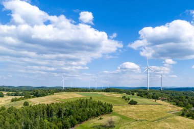 Parlak mavi gökyüzüne karşı yemyeşil tarlalar ve rüzgar türbinlerinin yer aldığı pitoresk bir manzara, yenilenebilir enerji ve doğal güzellik sergiliyor..