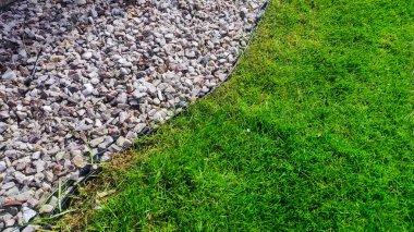 Manikürlü yeşil çimenler ve çakıllar arasındaki zıtlığı gösteren canlı bir fotoğraf. Peyzaj, bahçıvanlık ve açık hava tasarım temaları için ideal.