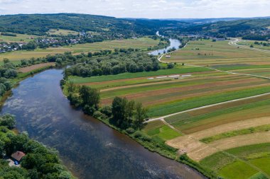 Bereketli yeşil bir manzaranın havadan görünüşü sergilenen tarlalar, dolambaçlı bir nehir ve parlak bir gökyüzünün altındaki uzak tepeler.