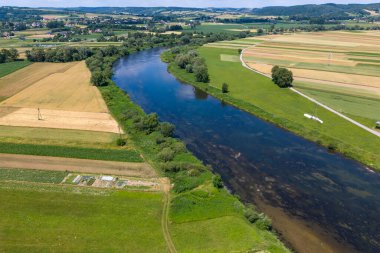Canlı yeşil tarlalar ve tarım arazileri boyunca kıvrılan sakin bir nehrin havadan görünüşü kırsal bölgenin güzelliğini gözler önüne seriyor..