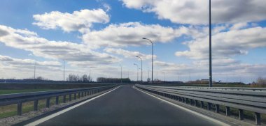 Pofuduk beyaz bulutlu, parlak mavi gökyüzünün altında manzaralı bir otoban manzarası. Dolambaçlı yol seyahat ve maceranın özünü yakalar..