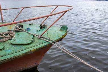 Suda dinlenen eski, yıpranmış bir teknenin yakın plan çekimi. Canlı yeşil boyası ve paslı metal detayları sergileniyor. Sakin su teknelerin eşsiz renklerini yansıtıyor..