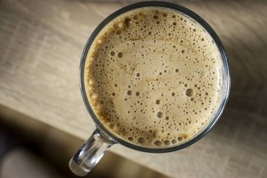 Köpüklü bir kahve fincanının üst görüntüsü ahşap bir yüzeyde dinleniyor, kremalı dokusunu ve davetkar görünümünü sergiliyor..