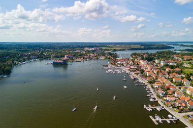 Mikoajki, Mazury 'nin hava manzarası, yemyeşil ve teknelerle çevrili, turizm ve eğlence faaliyetleri için mükemmel, pitoresk göl kenarı köyünü gösteriyor..