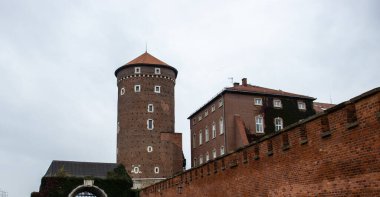 Bulutlu bir gökyüzüne karşı yuvarlak bir kule ve tuğla bir duvarın yer aldığı tarihi bir bina mimari detaylar ve sarmaşık kaplı duvarlar sergiliyor..