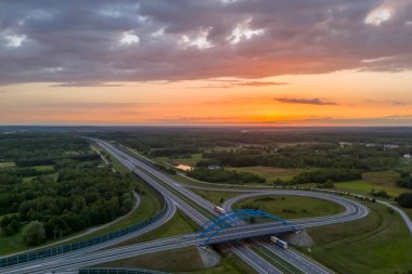 Karayolları ve yemyeşil çimlerin üzerinde gün batımı olan manzaralı bir manzara.