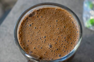Cam bardaktaki köpüklü sıcak çikolata zengin dokusunu ve köpüklü baloncuklarını gösteriyor. İçecek ve yemek fotoğrafçılığı için mükemmel..