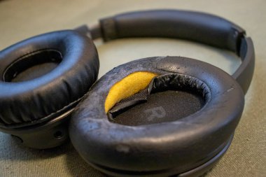 Close-up of worn-out black headphones with peeling ear cushions on a green background depicting wear and tear in everyday audio accessories. clipart