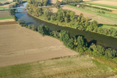 Tarlaların ve ağaçların arasında süzülen el değmemiş bir nehrin havadan görünüşü doğanın ve tarımın güzelliğini gösteriyor.