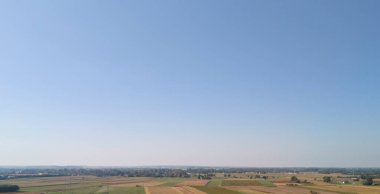 Açık mavi gökyüzünün altındaki sakin kırsal alanların panoramik görüntüsü doğa ve tarımın güzelliğini gözler önüne seriyor. Manzara ve doğa fotoğrafçılığı için mükemmel..