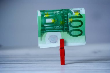 Finansal istikrar veya tasarrufu simgeleyen kırmızı bir mandalda 100 avroluk banknot bulanık bir arkaplan karşısında sergileniyor.