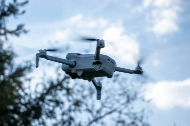 Aydınlık bir günde açık havada uçan bir İHA 'nın yakın çekimi. Arka plan, ağaçların ve açık mavi gökyüzünün doğada bir açık hava teknolojisi yarattığını gösteriyor..