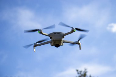 Aydınlık bir günde gökyüzünde uçan bir kuadkopter insansız hava aracının yakın çekimi. Beyaz dron havada süzülüyor, pervaneleri açık mavi bir arka planda dönüyor..