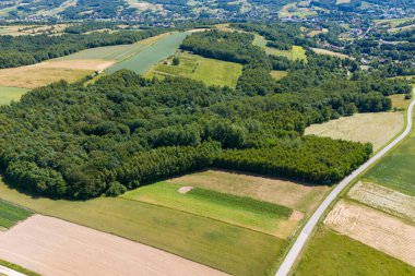 Aerial view of a rural landscape with forests fields and roads. The image shows a peaceful countryside with agricultural land and rolling hills under a clear sky.