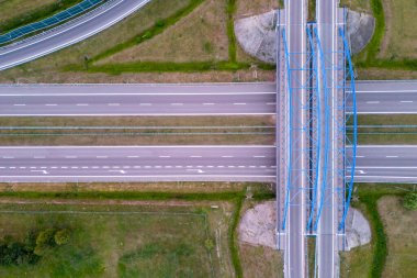 Çelik köprüsü ve çevreleyen yeşilliği olan boş bir otoyol kavşağının havadan görüntüsü. Açık yollar ve manzara, şehir altyapısına tepeden tırnağa bir perspektif sunuyor.