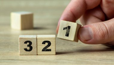 3 ve 2 numaralı blokların yanında 1 numaralı tahta blokları tutan bir el saymayı veya yaratıcı minimalist bir ortamda ilerlemeyi sembolize eder..