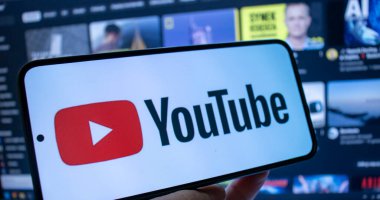 Varşova Polonya - 20 Eylül 2024: YouTube logosunu arka planda bulanık gösteren akıllı telefon taşıyan kişi. Teknoloji ve sosyal medya temaları için mükemmel.