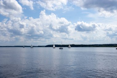 Mikolajki Polonya - 20 Eylül 2024: Bulutlu bir göl altında süzülen sakin bir yelkenli manzarası dinlenmek ve macera yaşamak için mükemmel bir cennet manzarası.