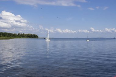 Mikolajki Polonya - 20 Eylül 2024: Mavi gökyüzü ve arka planda tüylü bulutlar sükunet ve maceraya davetiye çıkaran sakin bir göl üzerindeki yelkenli manzarası.
