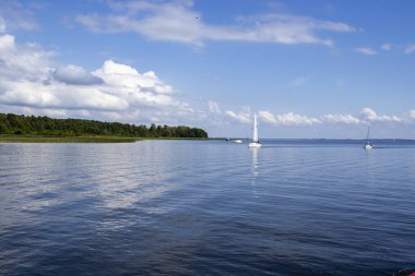 Mikolajki Polonya - 20 Eylül 2024: Bereketli yeşillik ve açık mavi gökyüzü ile çevrili sularda süzülen sakin bir göl manzarası.