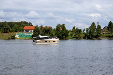 Mikolajki Polonya - 20 Eylül 2024: Bereketli yeşil manzaralarla çevrili sakin sularda gezinen lüks bir yat, yaz tatili ve dinlenme aktivitelerinin ruhunu yakalıyor..