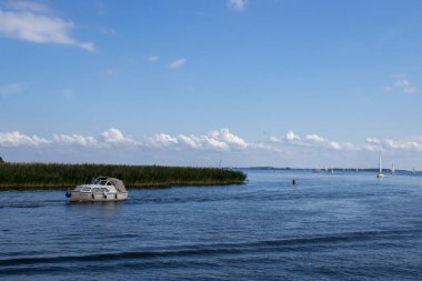 Mikolajki Polonya - 20 Eylül 2024: Bereketli yeşillik ve canlı mavi gökyüzü ile çevrili sakin sularda süzülen bir teknenin manzarası.