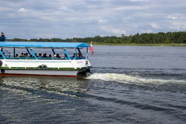 Mikolajki Polonya - 20 Eylül 2024: Bereketli yeşilliklerle çevrili sakin bir göl üzerinde gezinen bir teknenin manzaralı manzarası.