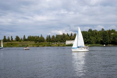 Mikolajki Polonya - 20 Eylül 2024: Bereketli yeşillikler ve bulutlu gökyüzüyle çevrili sakin sularda yüzen teknelerin manzarası