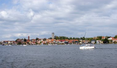 Mikolajki Polonya - 20 Eylül 2024: Mikolajki köyünün göl kenarındaki yelkenli tekneleri ve parlak gökyüzü altındaki büyüleyici evleri.